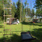 Een schommel en speelladder met daarachter twee campers omringd door bomen in Drenthe
