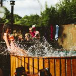Een houten hot tub waar de spetters uit vliegen en een spelend kind er in, op Camping BuitenLand