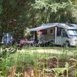 Een camper met luifel en mensen die voor de camper zitten op een natuurcamping in Drenthe