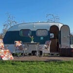 Een caravan met stoelen en een tafel ervoor op een camping in Friesland