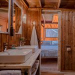 De houten badkamer met twee wasbakken en de deur naar een tweepersoons slaapkamer