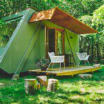 Forrest cabin met een veranda en 2 stoelen op een kampeerplek omringd door bomen op camping Het Bos Roept!