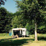 Caravan met luifel met twee personen ervoor op een camping in Noord-Holland