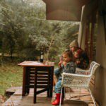 Cabin met een veranda waarop twee kinderen en een volwassene zitten