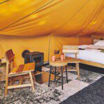 zithoek met houtkachel en een bed op de achtergrond in een ingerichte tent op natuurcamping Het Bos Roept!