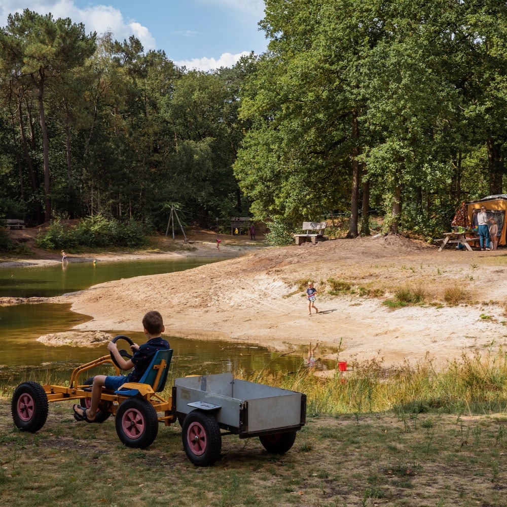 Jongen op een skelter rijdend naast een riviertje op een natuurcamping in Noord-Brabant