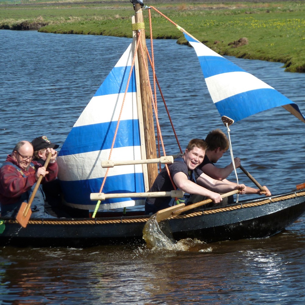 Jongeren hebben dikke pret in een zeilbootje met blauw witte zeilen