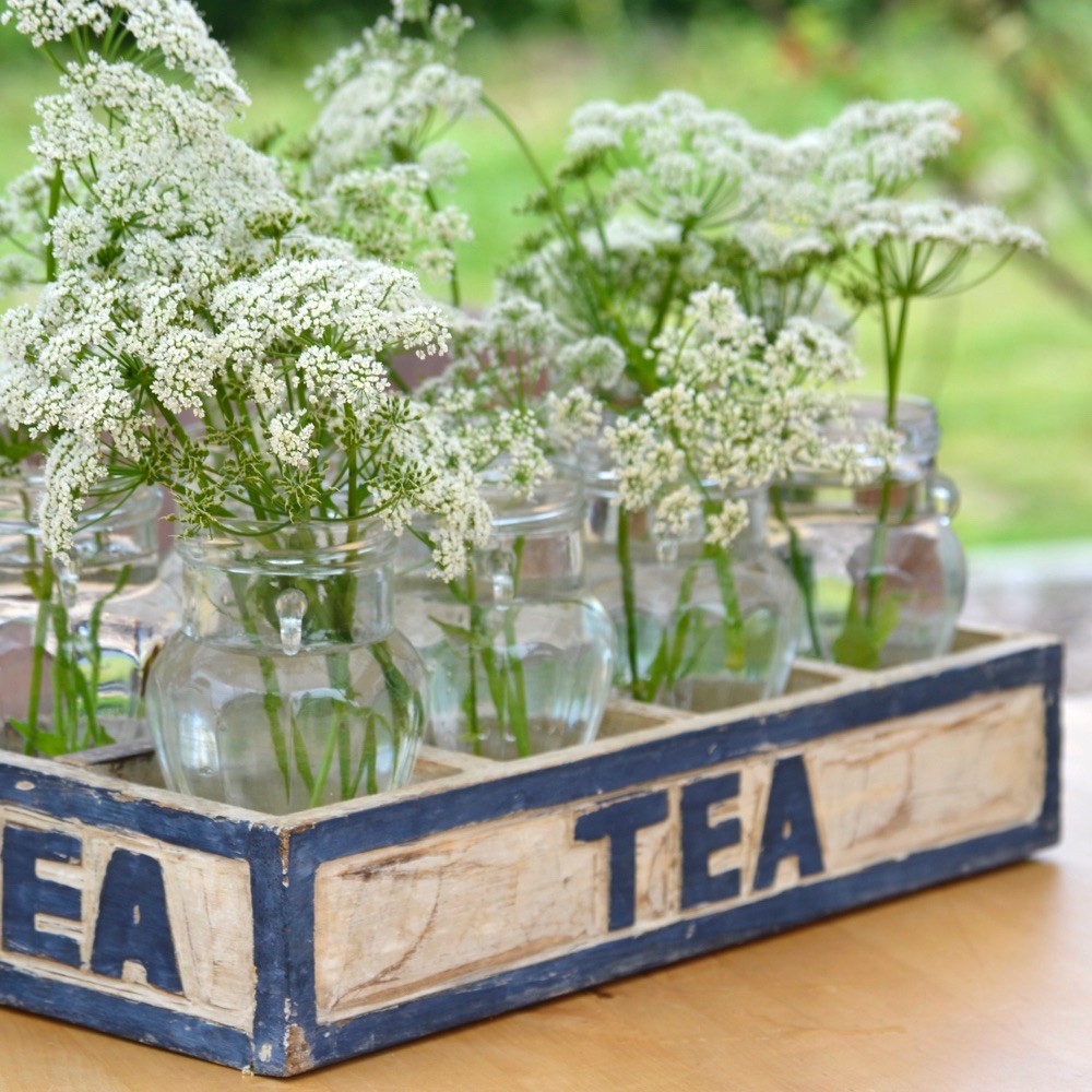 Witte veldbloemen in glazen flesjes in een houten kistje met TEA erop