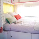 Opgemaakt bed in een van de huurcaravans, met wit beddengoed en gekleurde kussens