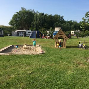 Kampeerveld met caravans, camper, zandbak en spelende kinderen
