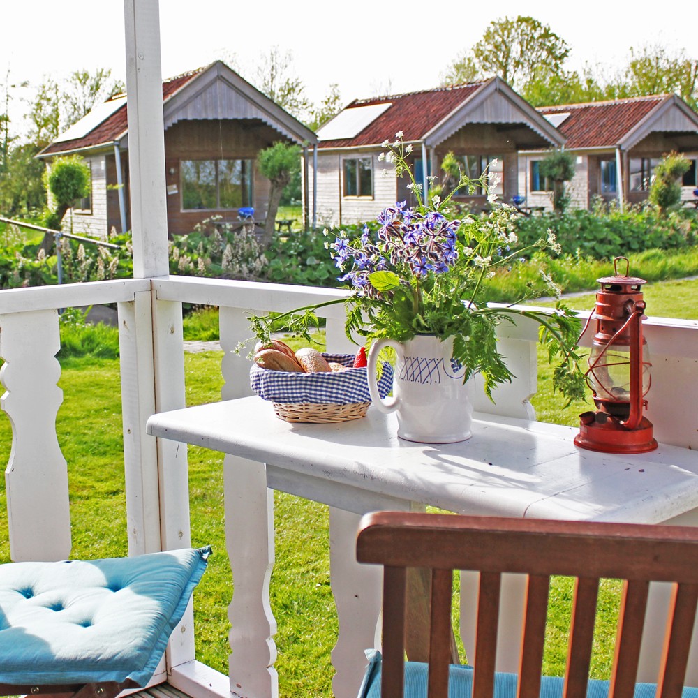 Een veranda met wit tafeltje, zomerse bloemetjes en een rode lantaarn