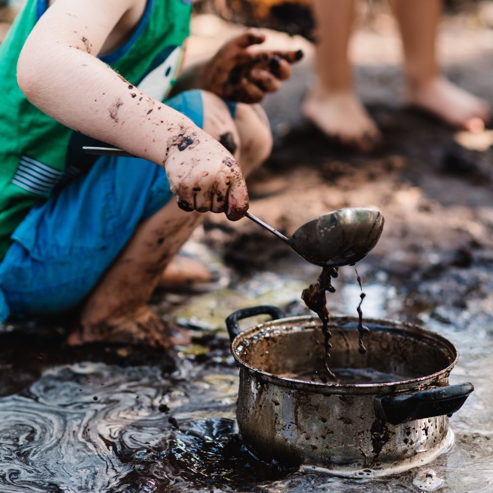 Een kind speelt met pan en soeplepel in de modder