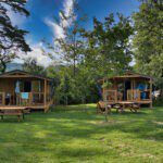 Twee ecolodges met picknicktafels ervoor op een groen kampeerveld op Camping Le Plô