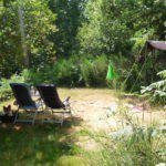 Ruime kampeerplaats op Camping Domaine Le Peyral, met twee kampeerstoelen op een open veldje omringd door groen.