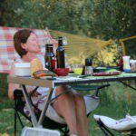 Vrouw aan een kampeertafel met een glas wijn
