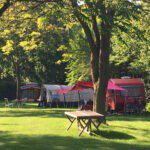 Rode caravan met luifel met een tent op de achtergrond op camping De Zoete Aagt