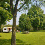 Caravan met luifel op een groen kampeerveld met bomen erop op camping De Zoete Aagt