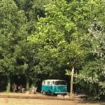 Volkswagen busje met mensen ernaast en bomen eromheen op Camping La Vaugelette