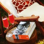 Stoel met een tafeltje ernaast met een boek, drankjes en een zonnebril erop