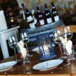 Gedekte tafel met op de achtergrond wijnflessen en een wijnvat