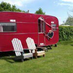 Rode caravan met twee stoelen ervoor op een kampeerveld op Minicamping Op den Boender