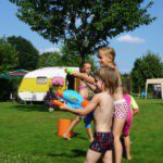 Spelende kinderen voor een geel witte caravan op een kindvriendelijke camping in Noord-
