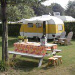 Geel witte caravan met luifel met een picknicktafel ervoor op Minicamping Op den Boender
