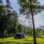 Groen kampeerveld met een tent erop omringd door bomen en uitzicht op Sloveense heuvels