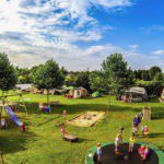 Overzicht van een groen kampeerveld met speelapparaten en tenten op Buitenplaats Drenthe