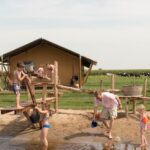 Kinderen spelend in een waterspeeltuin met een safaritent op de achtergrond