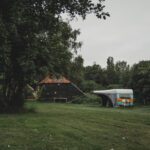 Caravan met een gebouw erachter op een groen kampeerveld in Drenthe