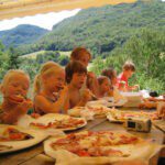 Kinderen aan tafel pizza aan het eten met daarachter groene heuvels in Frankrijk