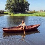 Vrouw in een boot aan het roeien in het landschap van het Groene Hart van Zuid-Holland