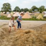 Twee kinderen spelend op het zand met op de achtergrond een glampingveld in Twente