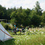 Tent met twee personen ervoor op een groen kampeerveld in het Vechtdal