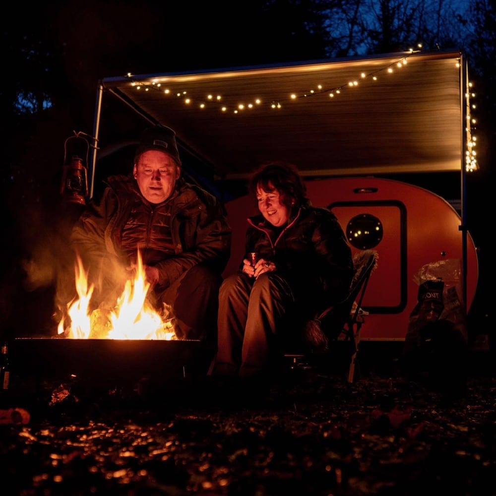 Man en vrouw voor een caravan met een vuurtje in de avond