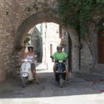 Twee volwassenen op een scooter in een oud Italiaans stadje