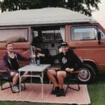 Man en vrouw proosten voor een camper bus van Volkswagen