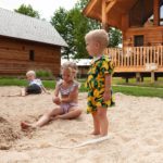 Drie kinderen spelen in het zand voor een houten lodge