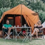 Man en vrouw voor een tent op een groen kampeerveld in het Oosten van Nederland