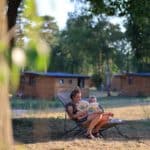 Vrouw leest zoon voor met op de achtergrond houten chalets op een glamping in Limburg